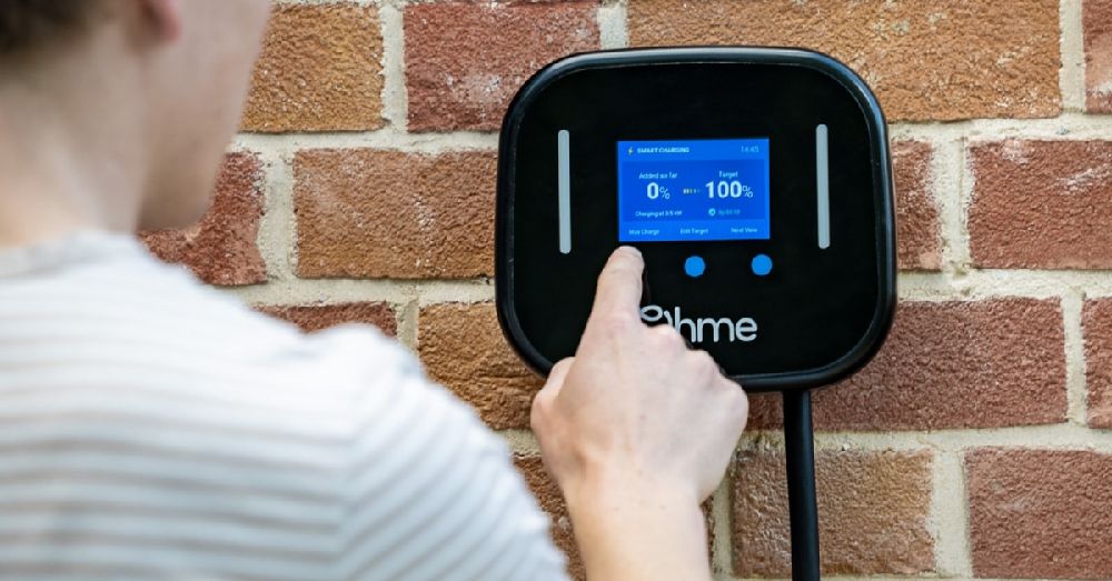 Person interacting with an Ohme Home Pro EV charger mounted on a brick wall, adjusting the smart charging settings on the digital display.